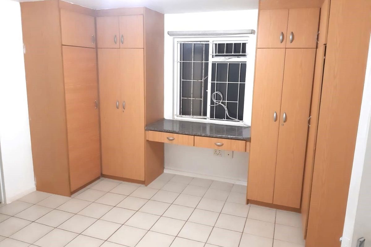 A functional bedroom featuring extensive built-in wooden cabinetry, a integrated desk area, tiled flooring, and a window fitted with security bars.