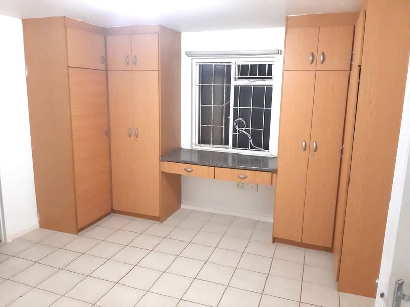 A functional bedroom featuring extensive built-in wooden cabinetry, a integrated desk area, tiled flooring, and a window fitted with security bars.
