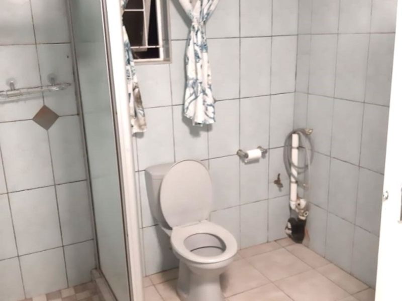 A functional bathroom featuring a shower enclosure, toilet, and tiled finishes. The space would benefit from cosmetic updates to modernize the fixtures and tiling.
