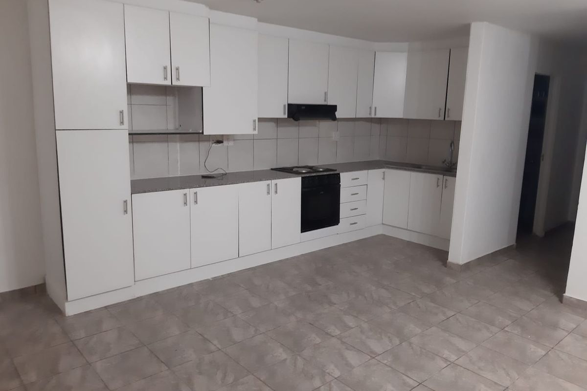 A clean, functional kitchen featuring white built-in cabinetry, a dark countertop, integrated oven and hob, and neutral tiled flooring.