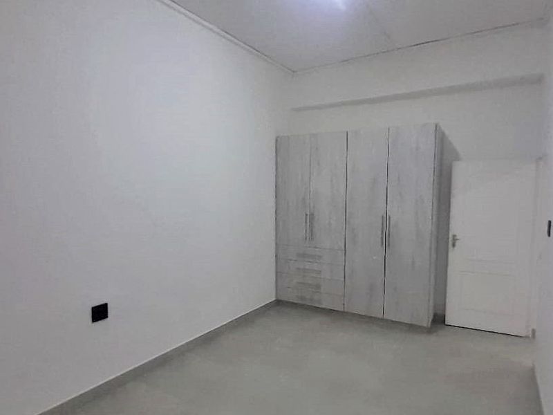 A clean, empty bedroom featuring a modern built-in wardrobe with light wood-grain finish and a standard internal door.
