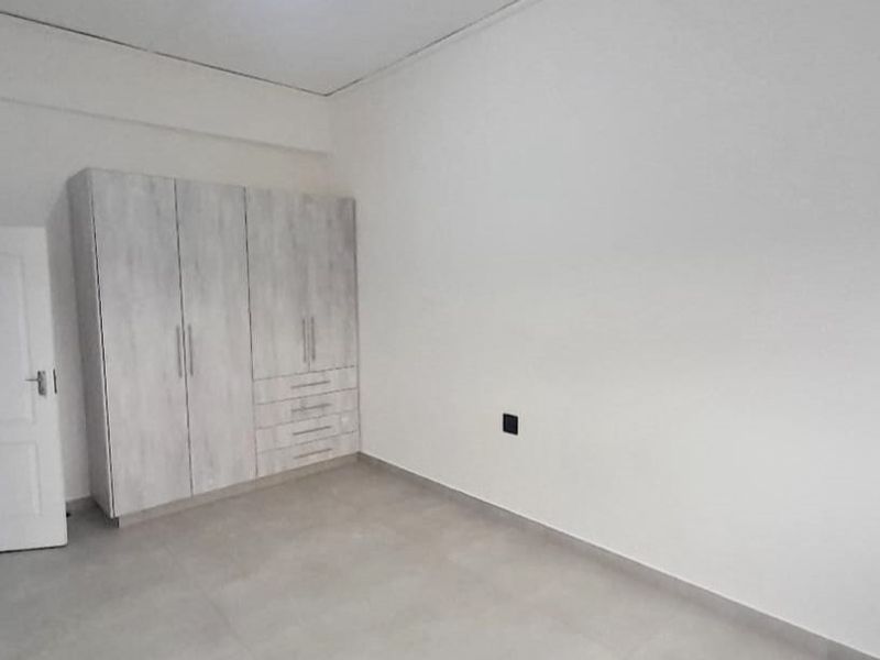A clean, empty bedroom featuring neutral tiled flooring and a modern built-in wardrobe with ample storage space.