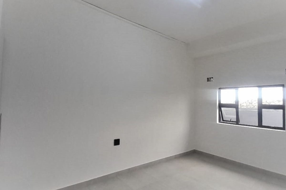 A bright, empty bedroom featuring neutral tiled flooring, a built-in wardrobe, and an aluminium-framed window providing natural light.
