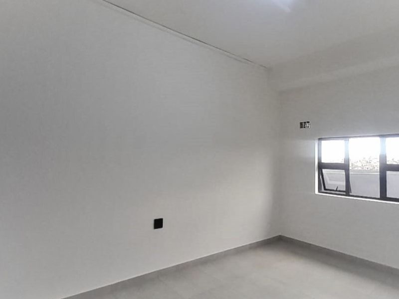 A bright, empty bedroom featuring neutral tiled flooring, a built-in wardrobe, and an aluminium-framed window providing natural light.