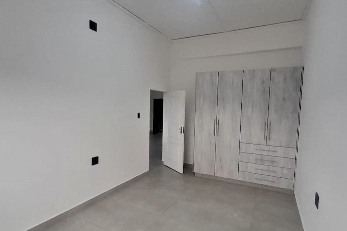 A clean, empty bedroom featuring neutral tiled flooring and modern built-in cupboards with ample storage space.
