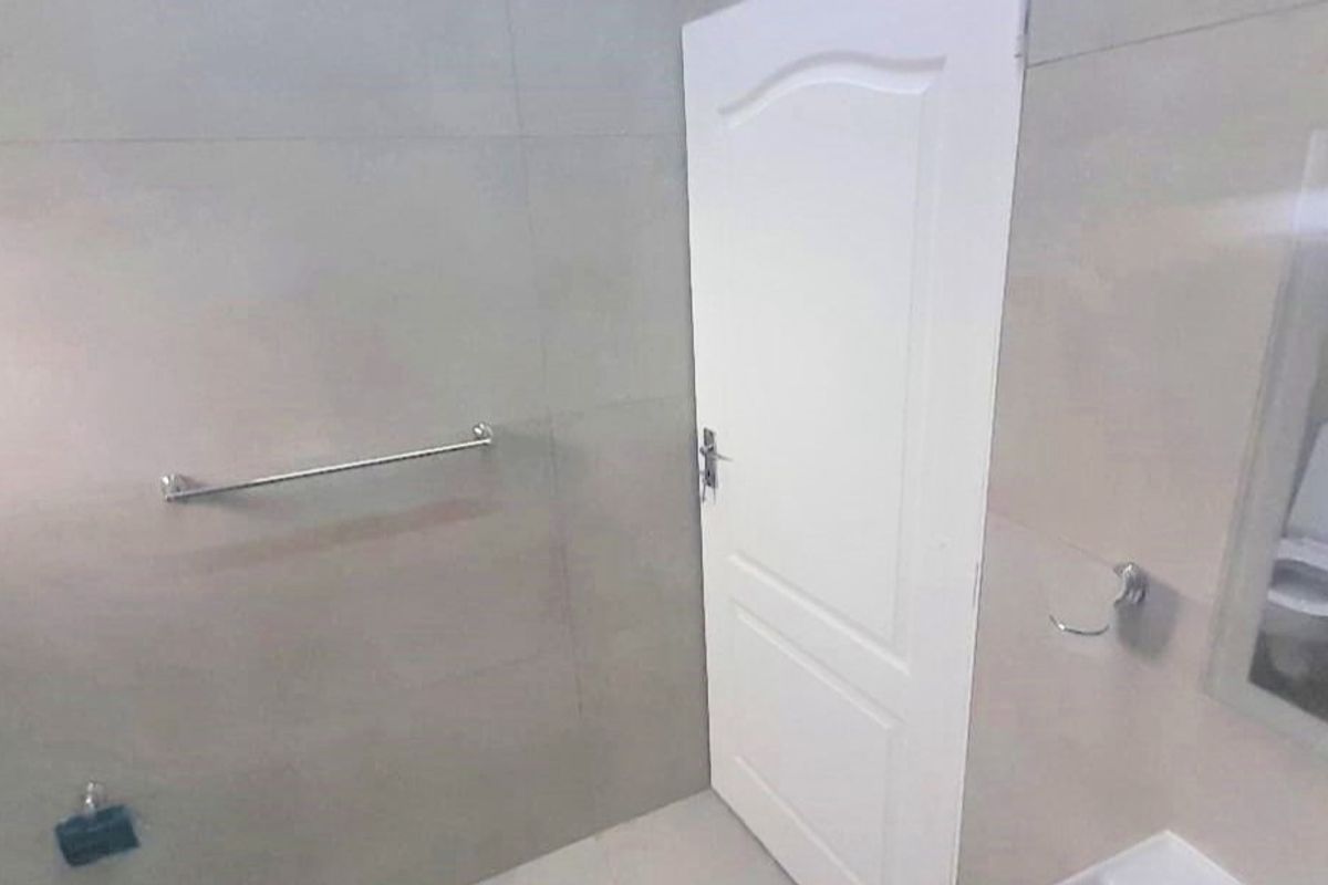 A clean, tiled bathroom featuring a wall-mounted towel rail, toilet roll holder, and a standard internal door.