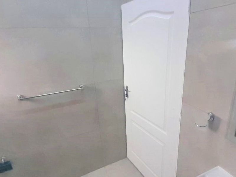 A clean, tiled bathroom featuring a wall-mounted towel rail, toilet roll holder, and a standard internal door.