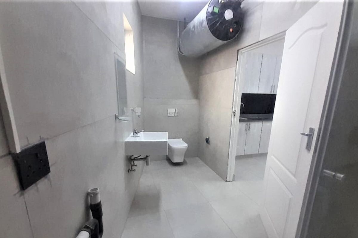 A minimalist bathroom featuring a wall-mounted basin and toilet, with exposed water heater and unfinished wall sections requiring cosmetic completion.