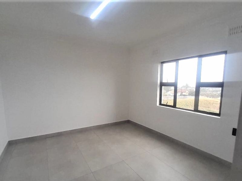 A clean, empty bedroom featuring neutral tiled flooring, white walls, and a large aluminium-framed window providing natural light.