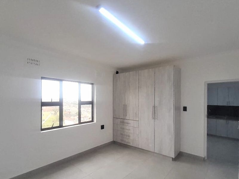 A bright, empty bedroom featuring neutral tiled flooring, built-in cupboards, and an aluminium-framed window with views.