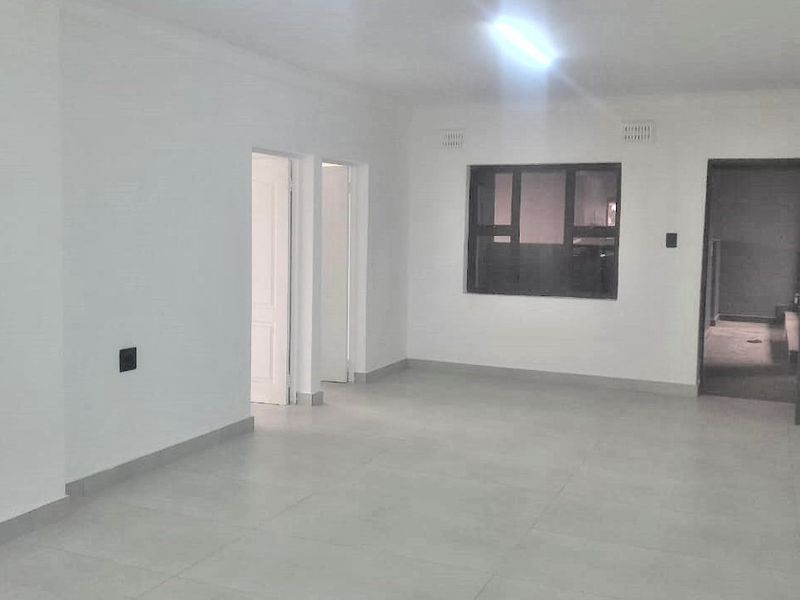 A bright, empty living area featuring neutral tiled flooring, clean white walls, and an aluminium-framed window, offering a blank canvas for interior design.