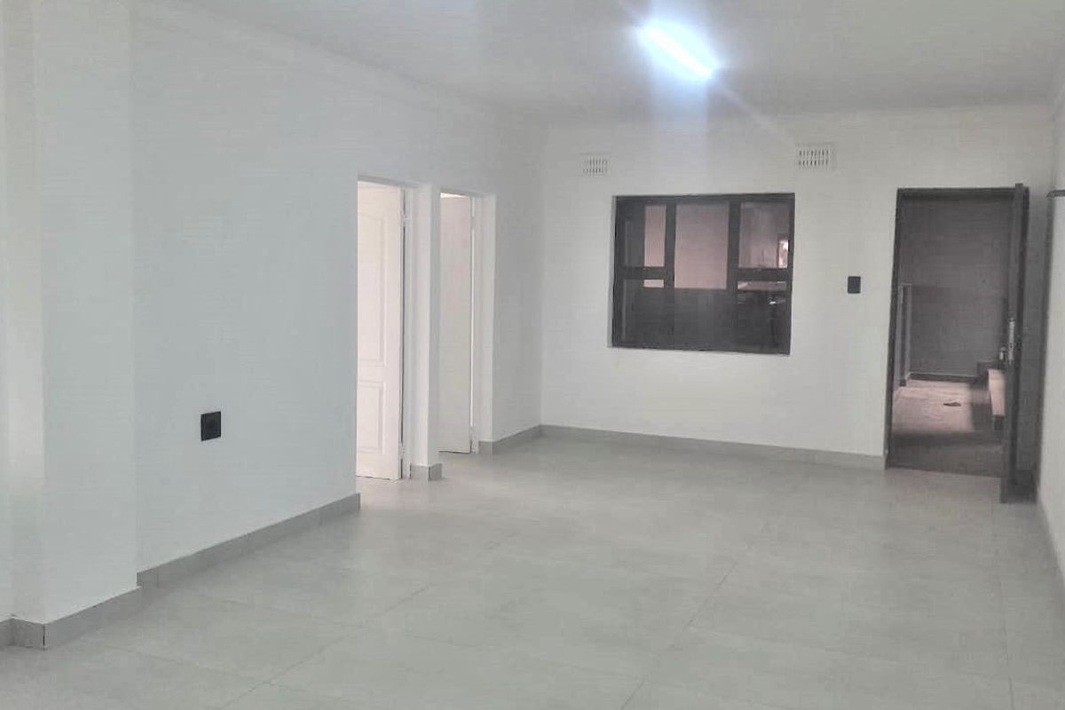A bright, empty living area featuring neutral tiled flooring, clean white walls, and an aluminium-framed window, offering a blank canvas for interior design.