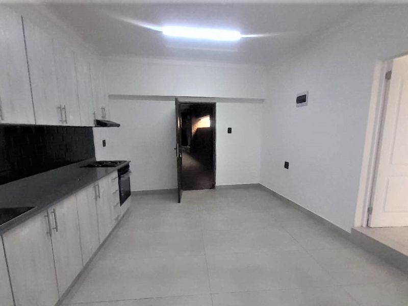 A clean, empty kitchen featuring light-toned built-in cabinetry, a dark countertop, a built-in oven and hob, and modern tiled flooring.