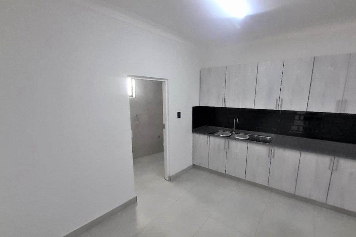 A clean, empty kitchen featuring white built-in cabinetry, a black splashback, and a double sink with tiled flooring.