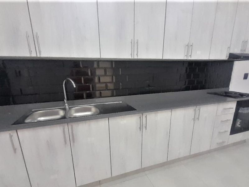Modern kitchen featuring light wood-grain cabinetry, a sleek black subway tile backsplash, stone countertops, and integrated appliances including an oven and hob.