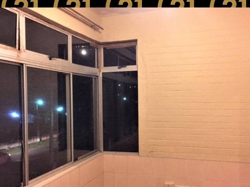 An enclosed balcony or sunroom featuring large aluminum-framed windows and tiled wall accents, currently in need of cosmetic refurbishment.