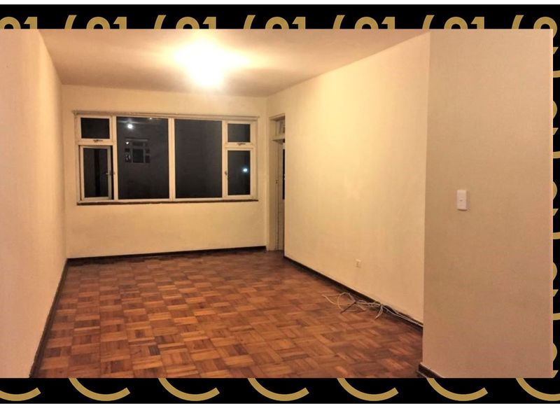 An empty living room featuring original parquet flooring and a large window, providing a blank canvas for renovation and interior design.