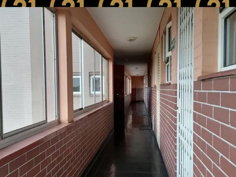 A long apartment hallway featuring brick walls, large sliding windows, and a security gate entrance.