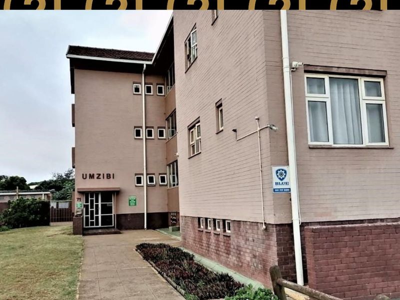Exterior view of the Umzibi apartment building featuring a brick facade, paved entrance walkway, and security infrastructure.