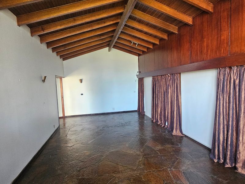 Spacious living area featuring a vaulted timber beam ceiling, unique flagstone flooring, and warm wood wall paneling, offering a character-filled blank canvas.