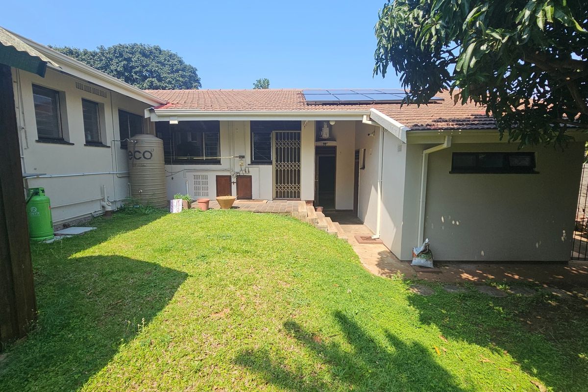 Rear view of the property featuring a lawn, paved patio, solar panels on the tiled roof, and an installed water storage tank.