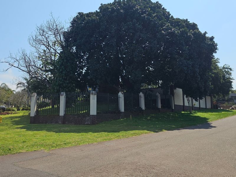 Street view of the property boundary featuring a brick and metal security fence surrounded by mature trees and a well-maintained lawn.