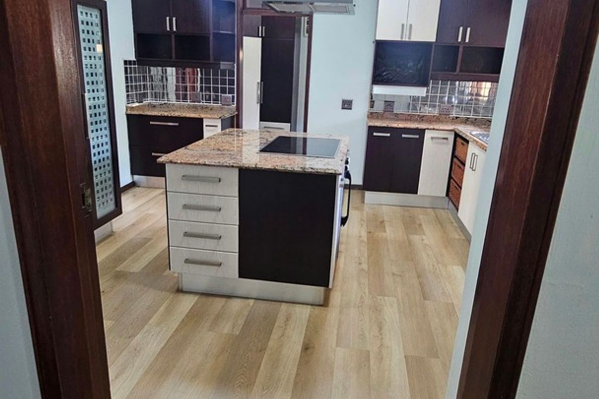 A modern kitchen featuring a central island with a built-in hob, granite countertops, dark and light cabinetry, and light-toned laminate flooring.