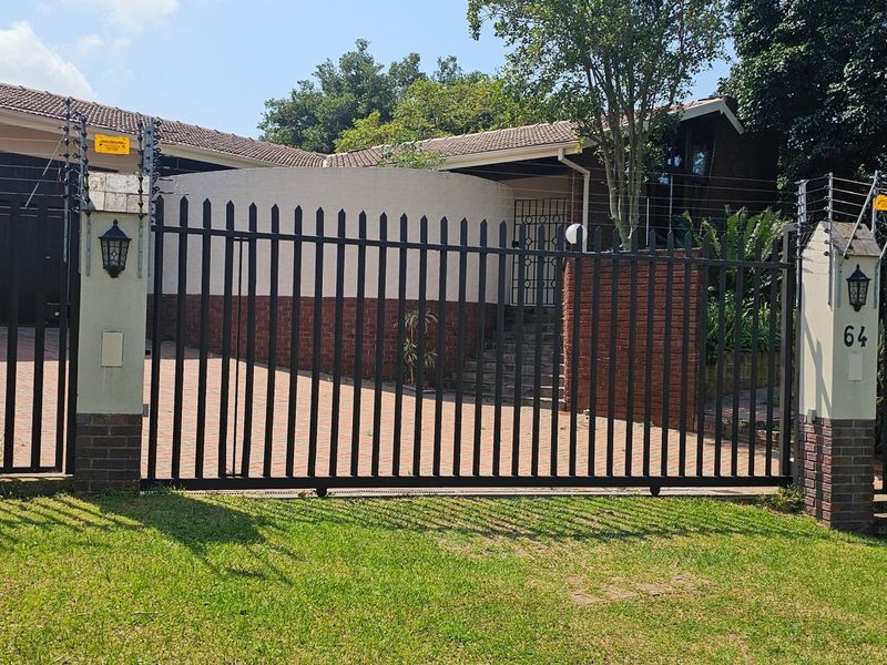 Front view of the property featuring a secure gated entrance, paved driveway, and perimeter electric fencing.