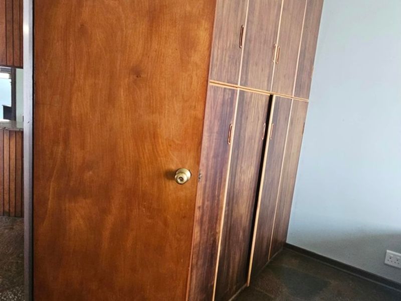 A bedroom featuring built-in wooden cupboards, stone flooring, and coved ceiling detailing, presenting a dated aesthetic in need of modernization.