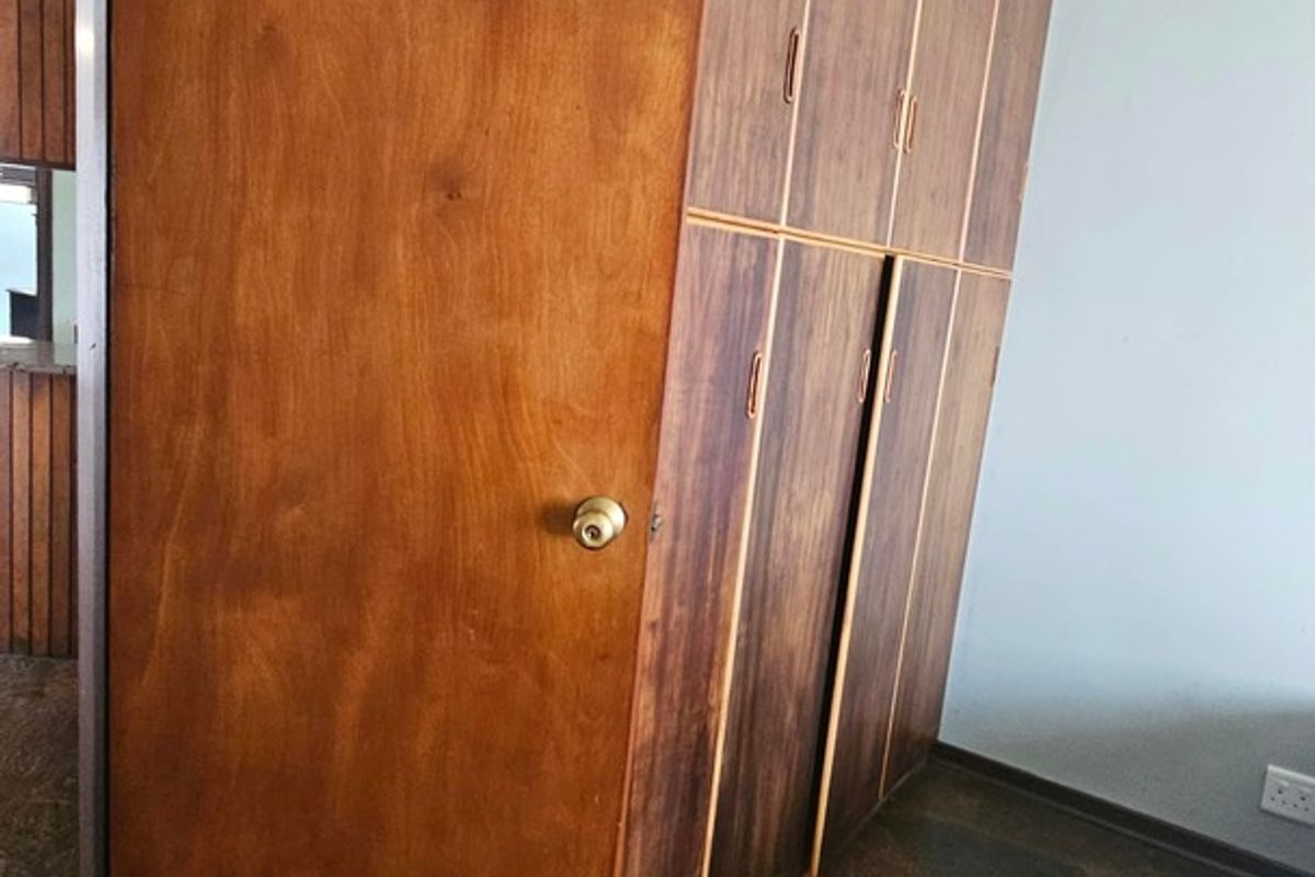 A bedroom featuring built-in wooden cupboards, stone flooring, and coved ceiling detailing, presenting a dated aesthetic in need of modernization.