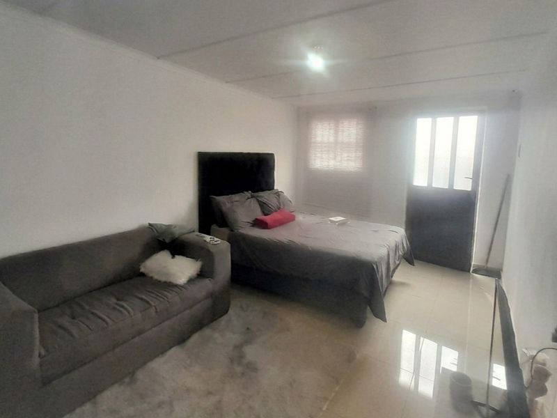 A functional bedroom featuring tiled flooring, a panelled ceiling, and direct access to the exterior via a glass-panelled door.