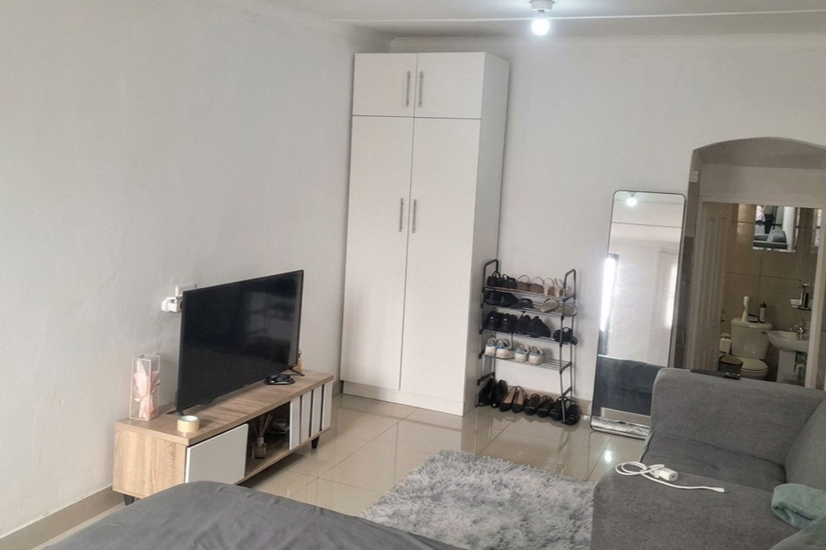 A living room featuring tiled flooring, a built-in wardrobe, and coved ceiling details, with an adjacent view into a bathroom area.