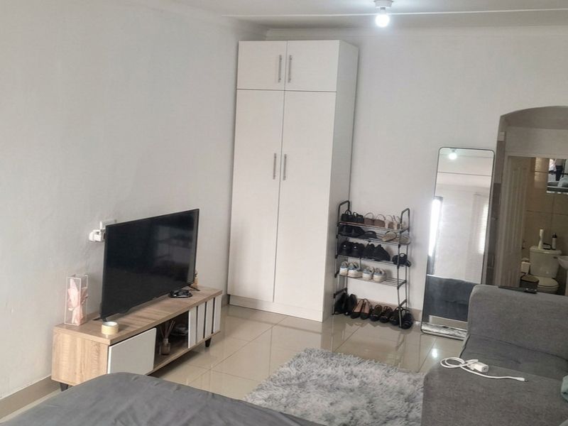 A living room featuring tiled flooring, a built-in wardrobe, and coved ceiling details, with an adjacent view into a bathroom area.