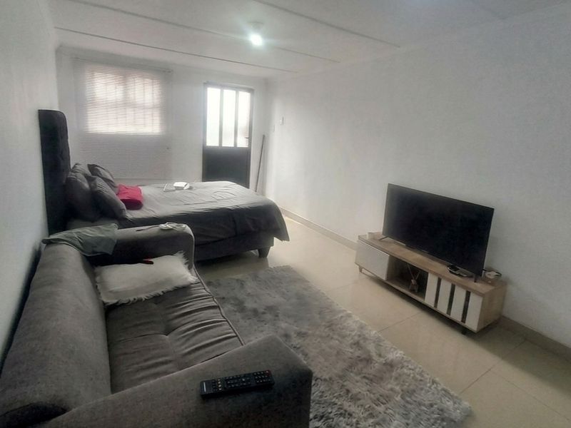 A functional bedroom space featuring tiled flooring, neutral walls, and direct access to an external door with fitted venetian blinds.