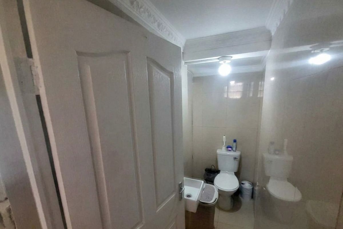 A compact bathroom featuring tiled walls, a wall-mounted basin, and a standard toilet, finished with decorative crown molding.
