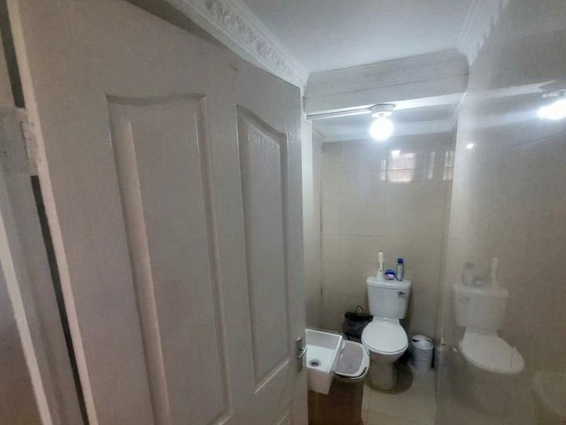 A compact bathroom featuring tiled walls, a wall-mounted basin, and a standard toilet, finished with decorative crown molding.