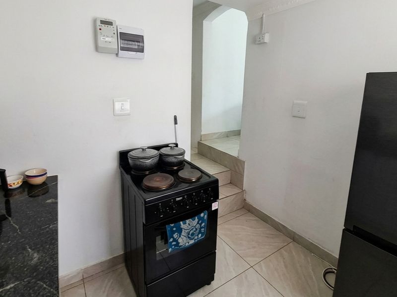 A functional kitchen area featuring tiled flooring, granite countertops, and a freestanding stove, with a step leading to an adjacent room.