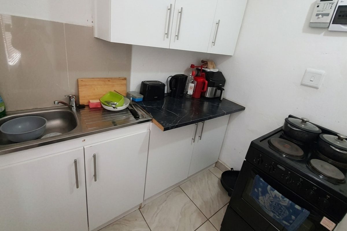 Compact kitchen featuring white cabinetry, dark laminate countertops, a stainless steel sink, and a freestanding electric stove with tiled flooring.