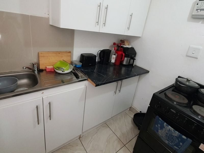 Compact kitchen featuring white cabinetry, dark laminate countertops, a stainless steel sink, and a freestanding electric stove with tiled flooring.