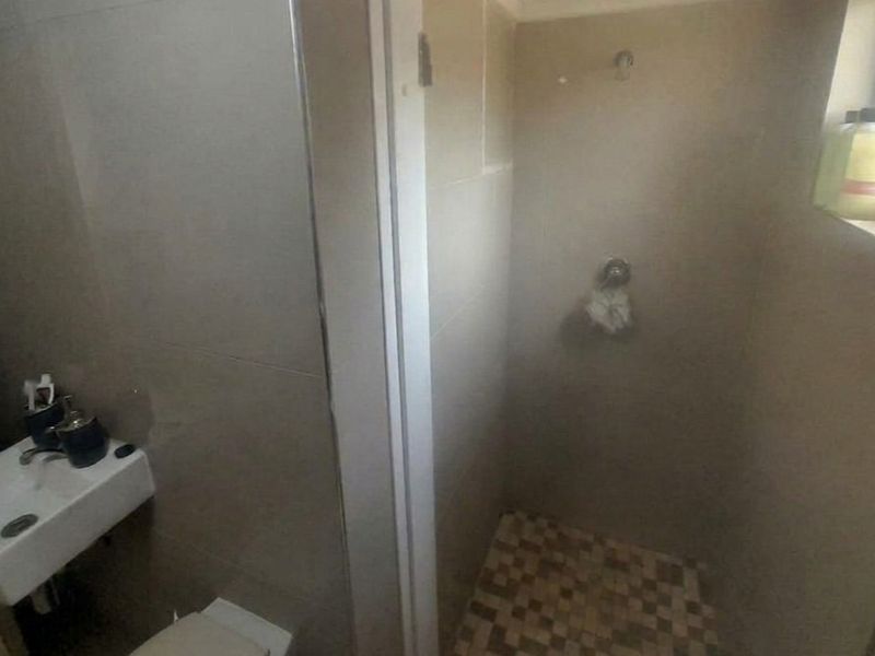 A compact bathroom featuring a wall-mounted basin and a shower enclosure with tiled finishes, currently requiring some maintenance and updates.