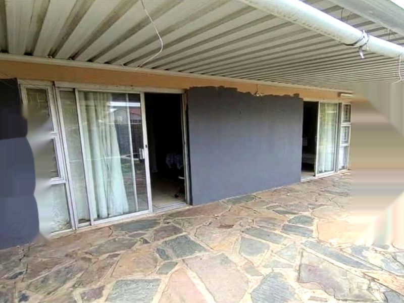 Covered patio area featuring stone paving and sliding glass door access to the interior, requiring cosmetic updates to the exterior wall finish.