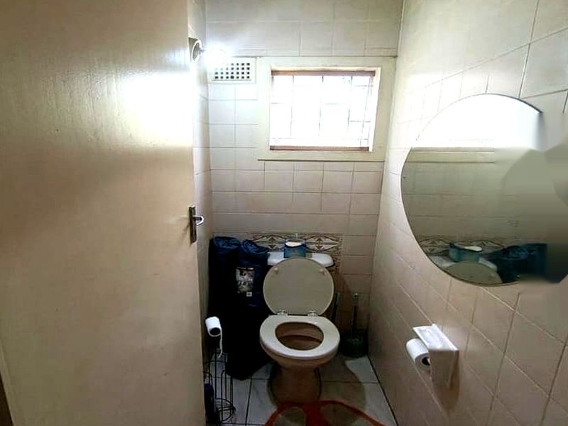 A compact bathroom featuring tiled walls and flooring, a standard toilet, and a small window for natural light and ventilation.