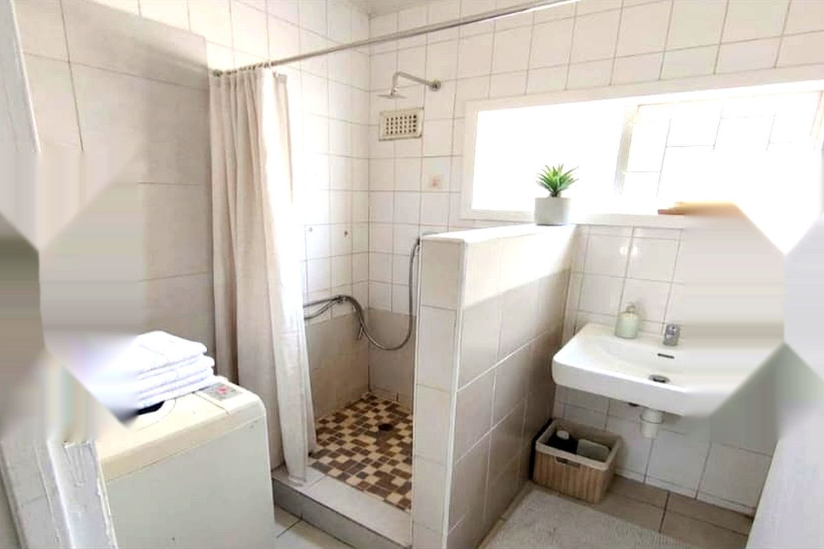 A functional bathroom featuring a shower area with tiled walls and a wall-mounted basin, requiring some maintenance and cosmetic updates.