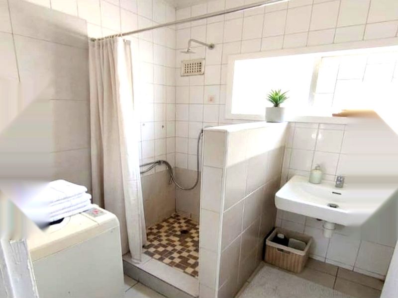 A functional bathroom featuring a shower area with tiled walls and a wall-mounted basin, requiring some maintenance and cosmetic updates.