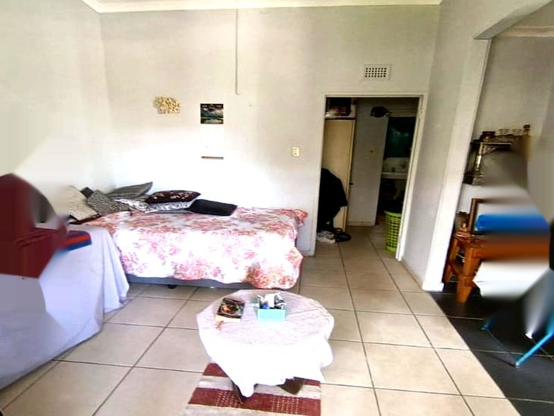 A bedroom featuring tiled flooring and a neutral wall finish, providing a functional space with direct access to an adjoining room.