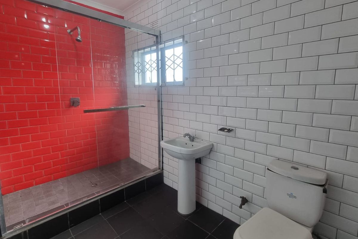 Modern bathroom featuring a glass-enclosed shower with red accent tiling, a white pedestal basin, and a toilet, finished with classic white subway wall tiles.