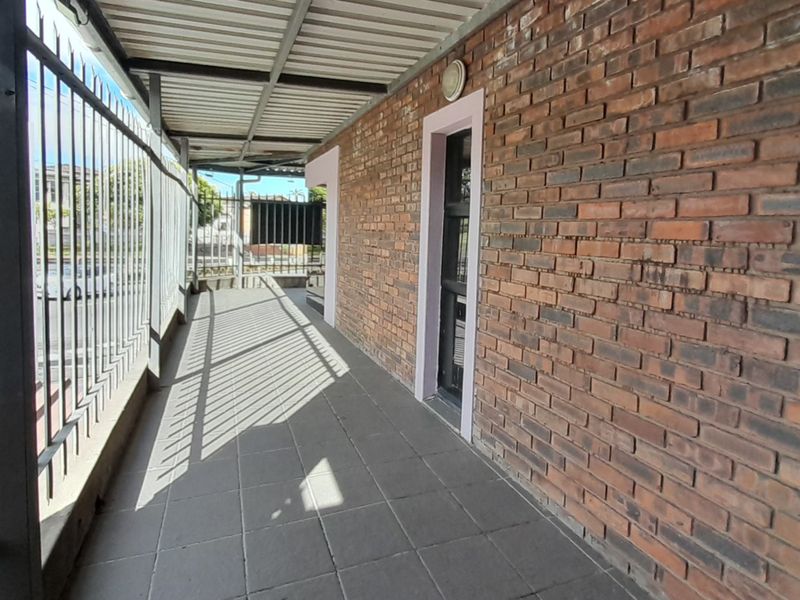 A covered outdoor patio area featuring exposed brick walls, tiled flooring, and secure metal fencing, providing a functional exterior transition space.