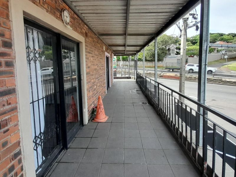 A covered outdoor balcony featuring exposed brick walls, tiled flooring, and a metal safety railing, overlooking the street.