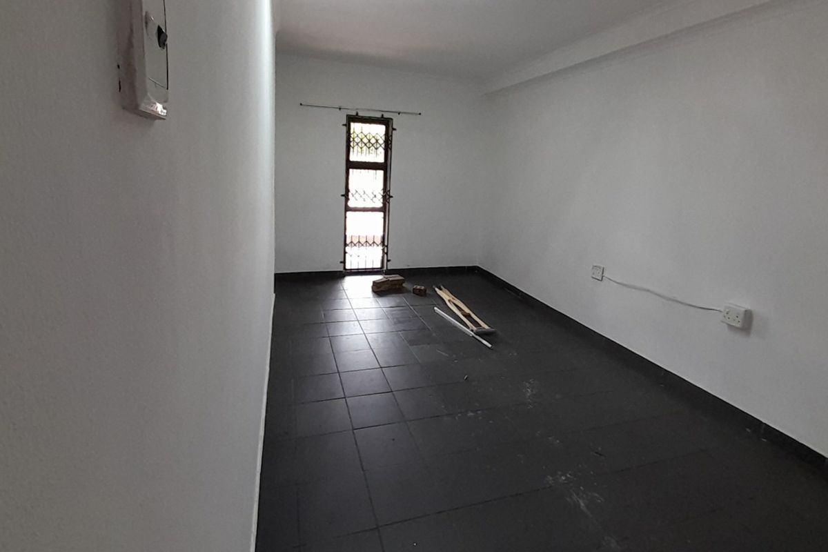 An empty bedroom featuring dark tiled flooring, white walls, and a security gate on the window.