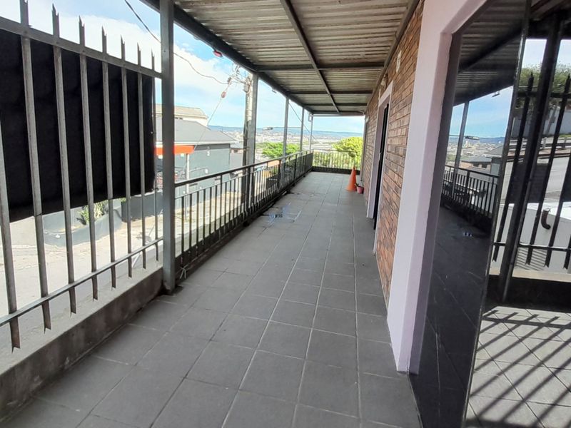 A covered outdoor balcony featuring tiled flooring, metal security fencing, and a corrugated roof, offering an elevated view of the surrounding area.